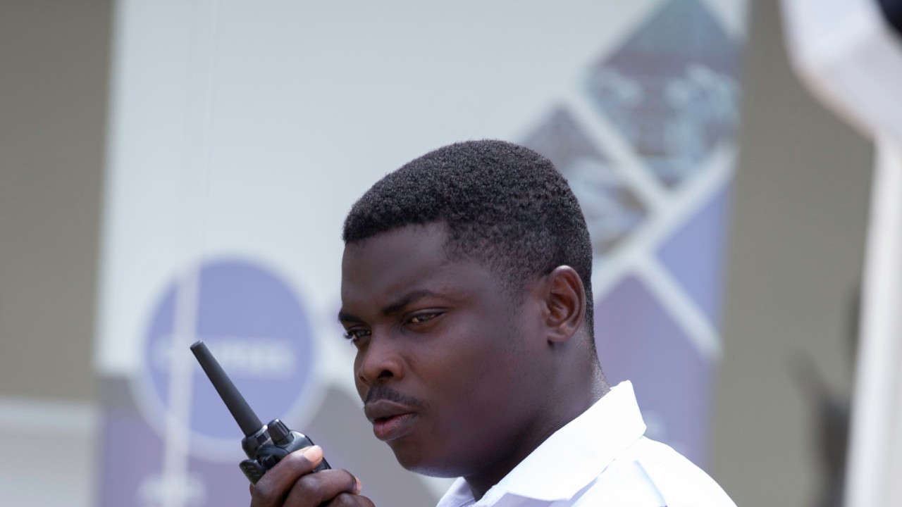 Offin Security officer in a white uniform shirt holding a two-way radio to his mouth at an event entrance